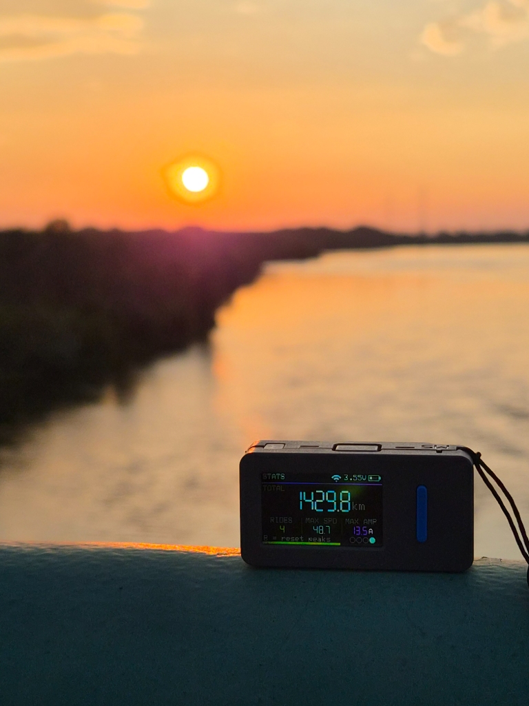 EucBuddy device with red lanyard on a wheel at sunset, showing 1429.8 km total and 48.7 km/h max speed